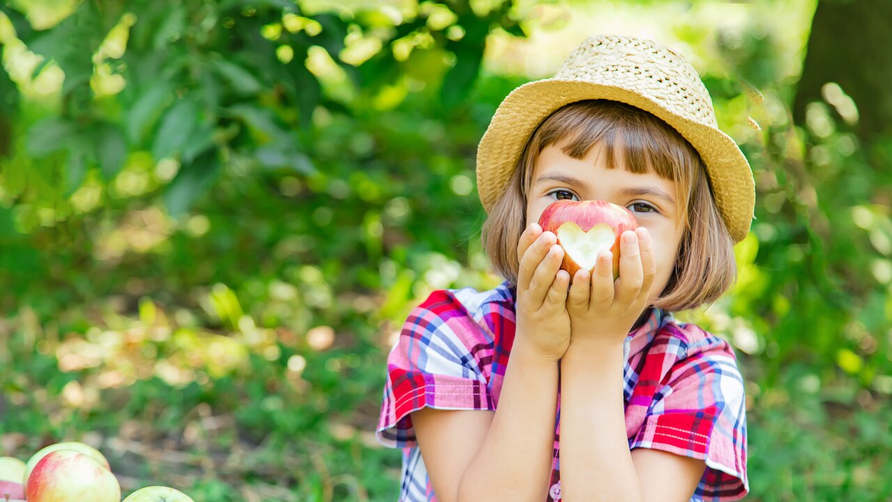 Ein Mädchen freut sich über einen Apfel, in den ein Herz geschnitzt wurde.