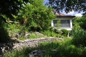 Überblick über den vielfältig gestalteten Garten mit grosser Trockenmauer und schattenspendenden Bäumen, die das Haus im Sommer auf natürliche Weise kühlen. | © Andermatt Biogarten AG